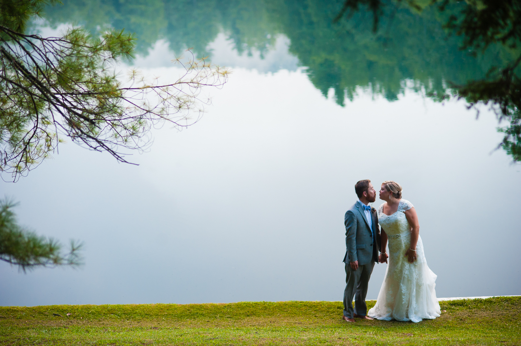 beautiful bride and groom kiss in front of a mountain lake with tree reflections