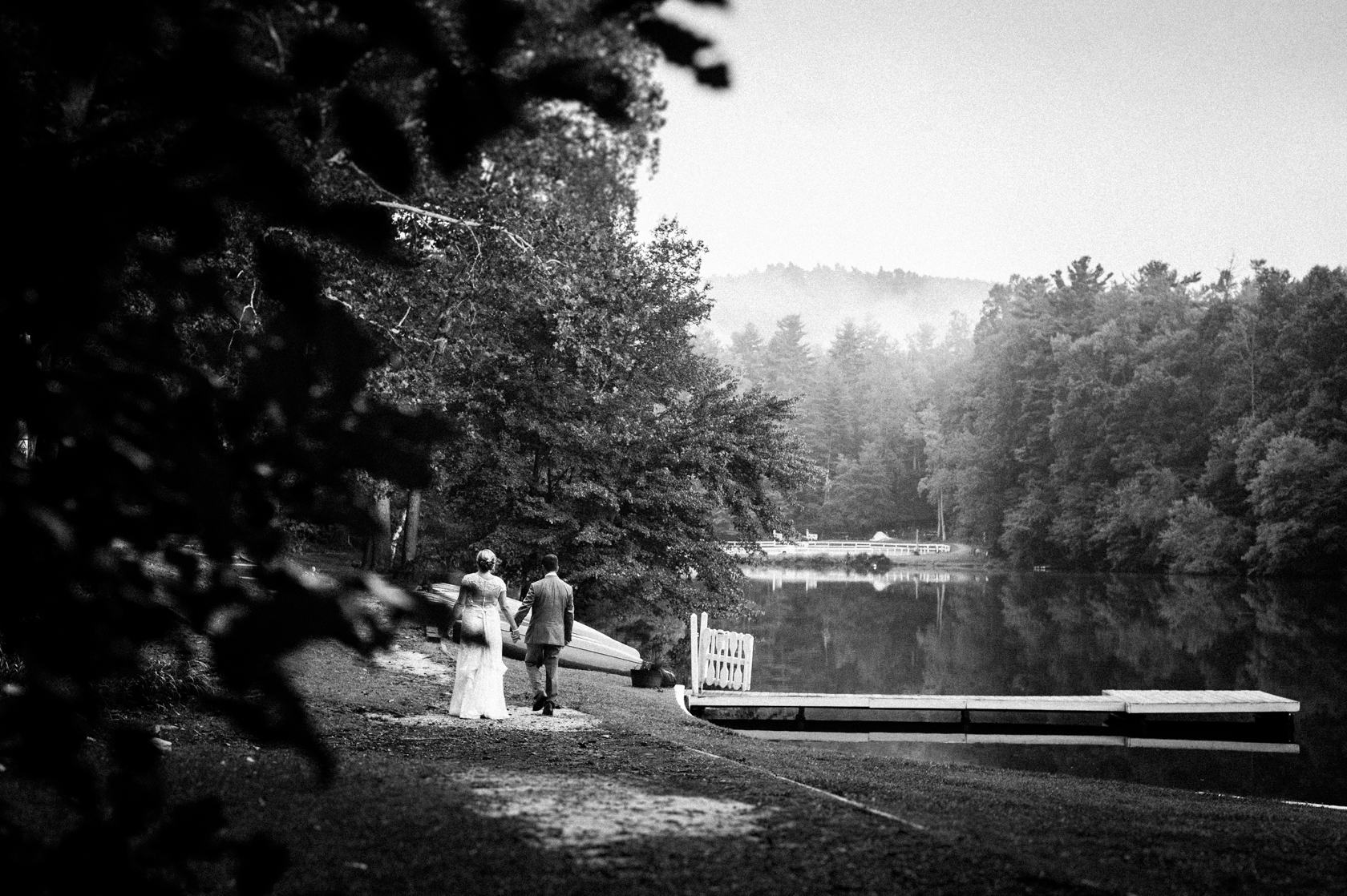 bride and groom walk hand in alongside a misty mountain lake 