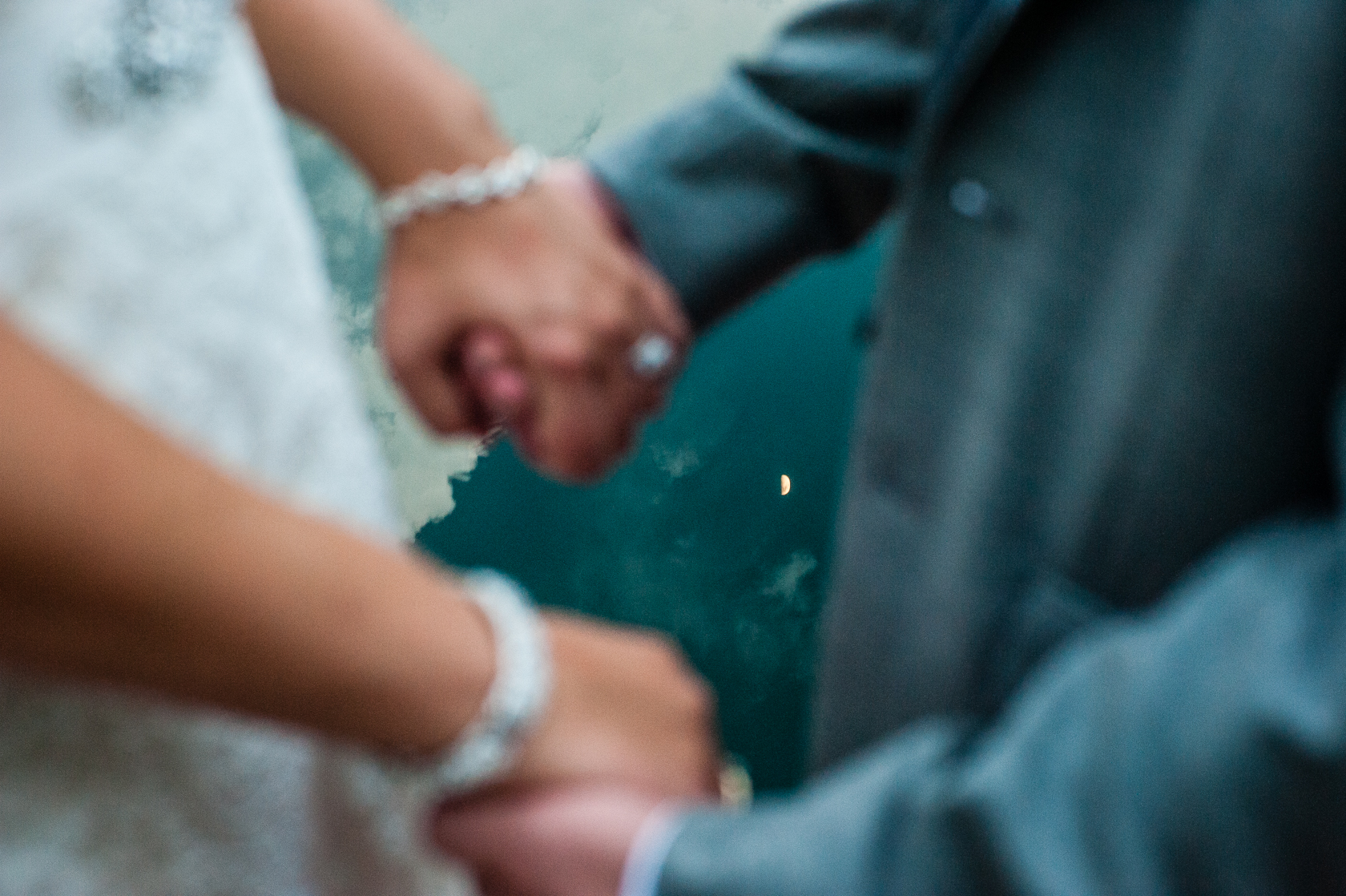 a close up of bride and grooms hands with the moon reflecting in the lake behind 