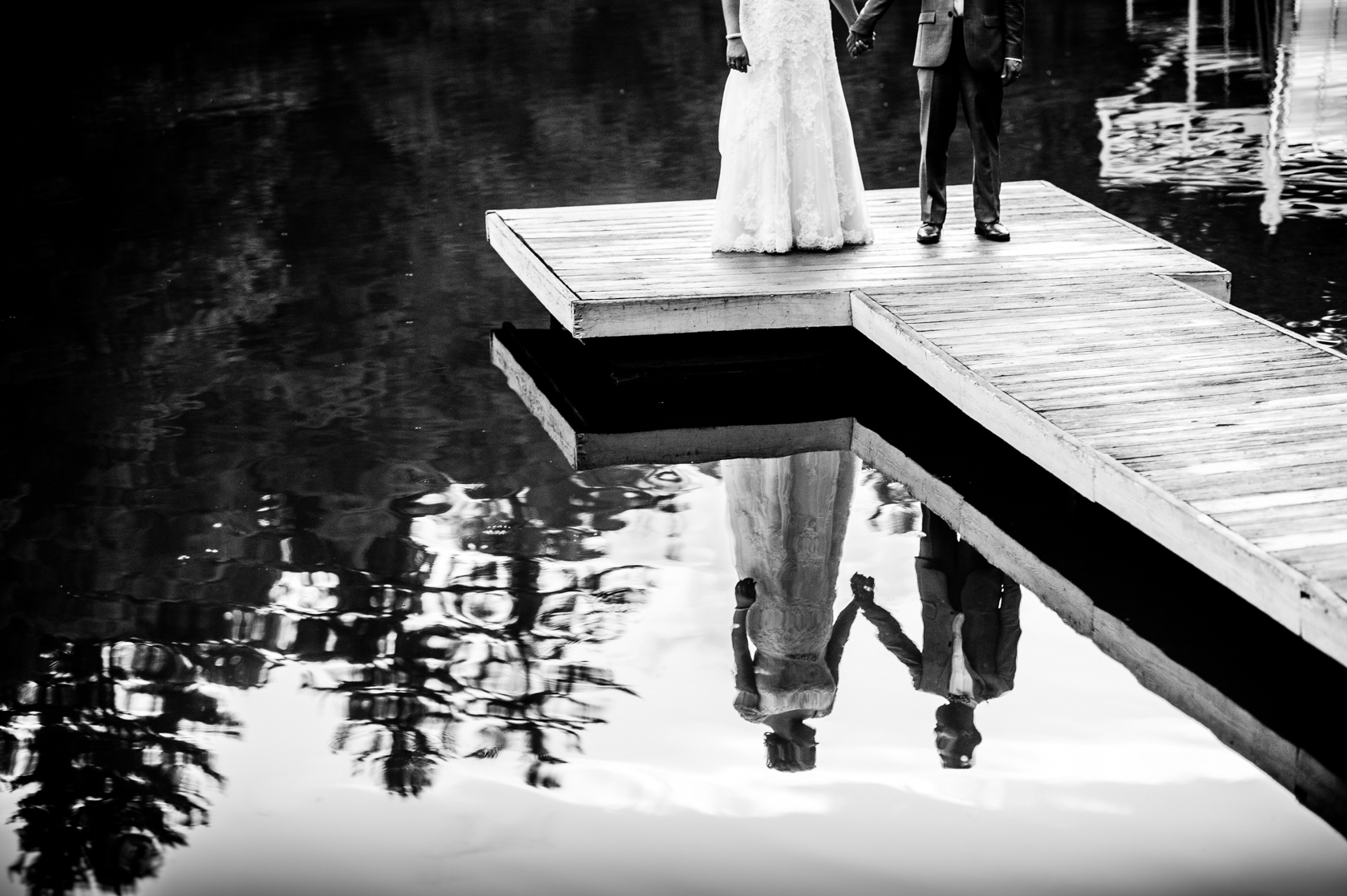 black and white reflection of bride and groom holding hands in mountain lake 