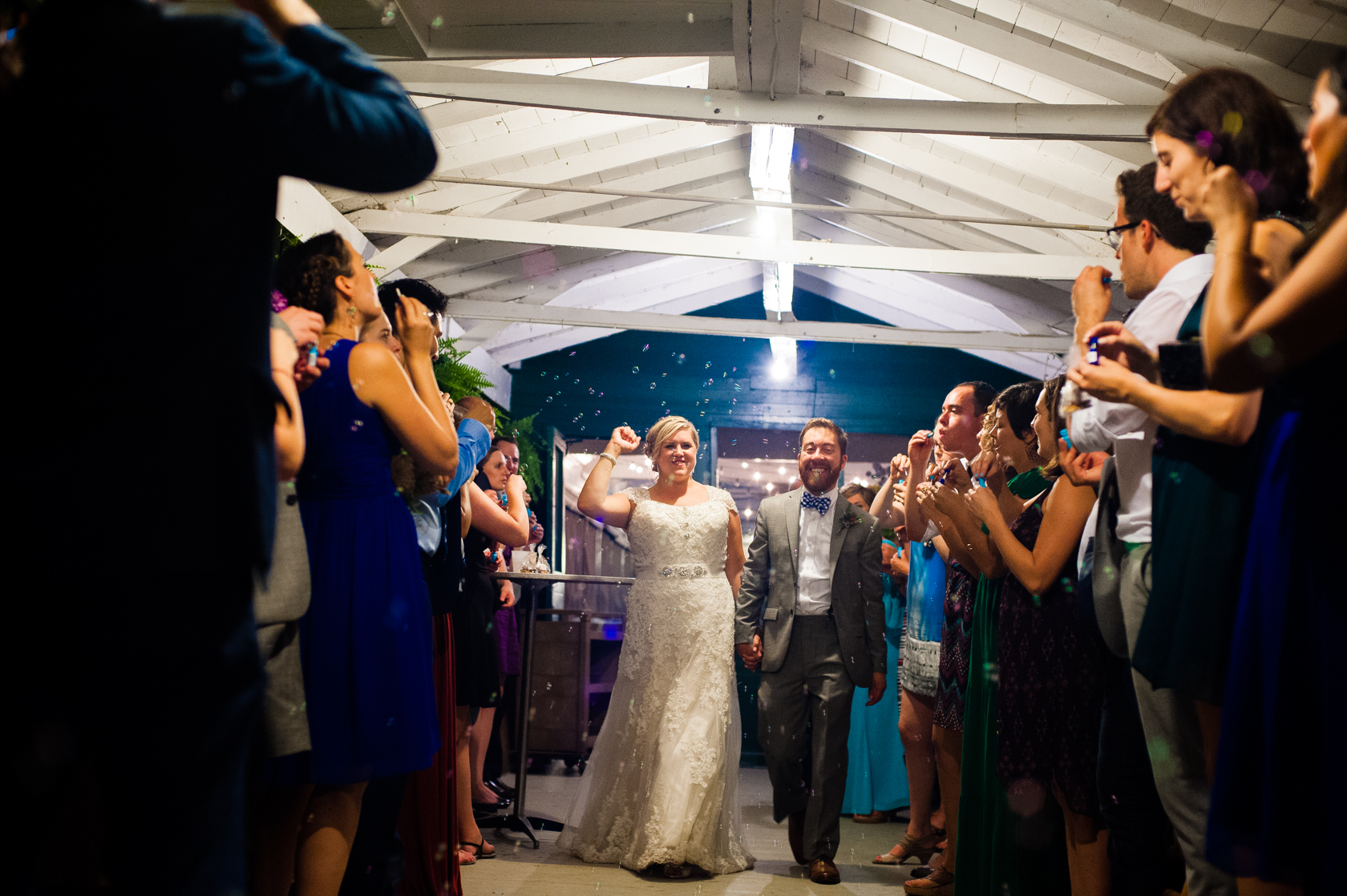 bride and groom run out of a summer camp mess hall with bubbles surrounding them