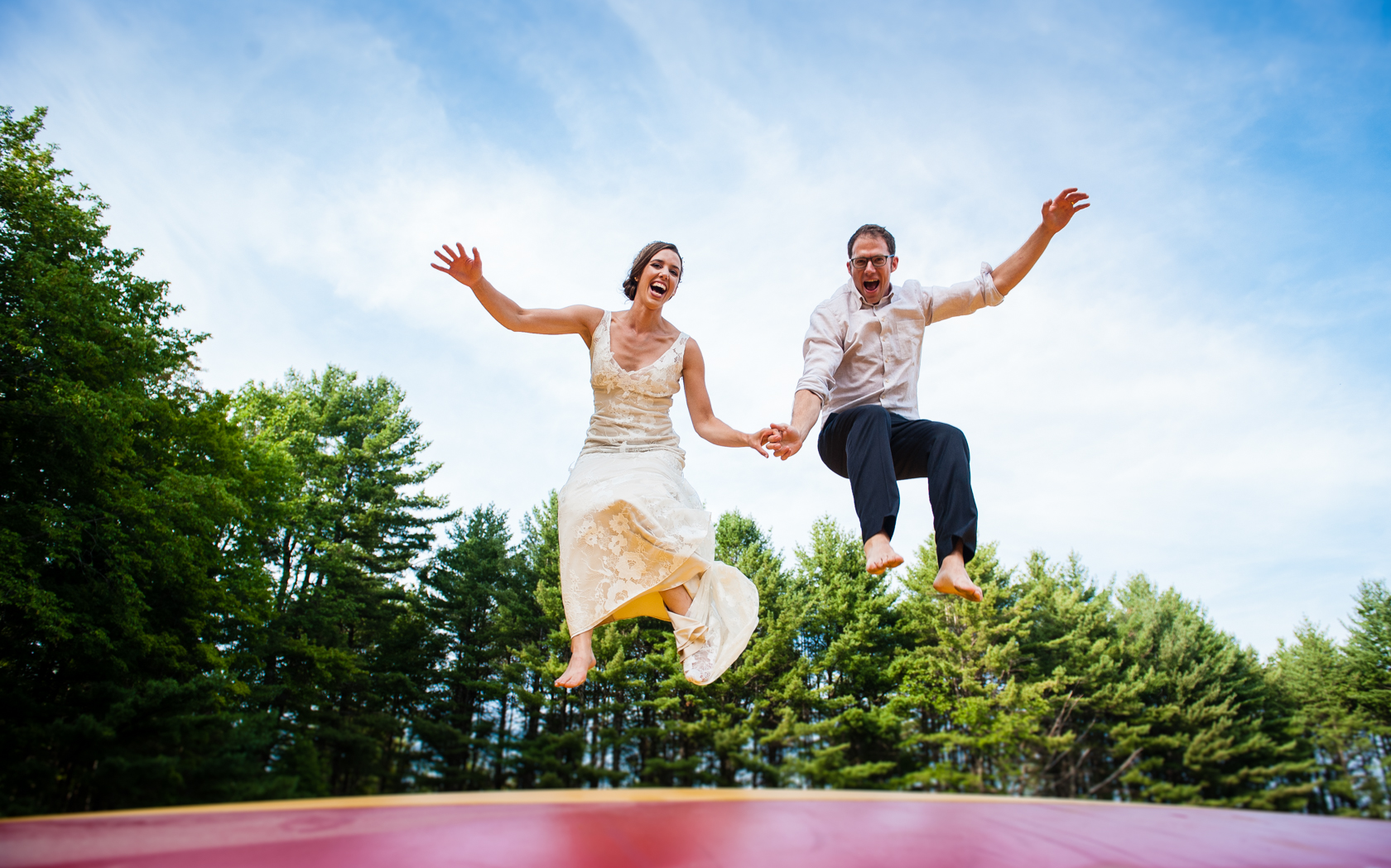 fun adventurous bride and groom jumping on a big air bounce in wedding attire