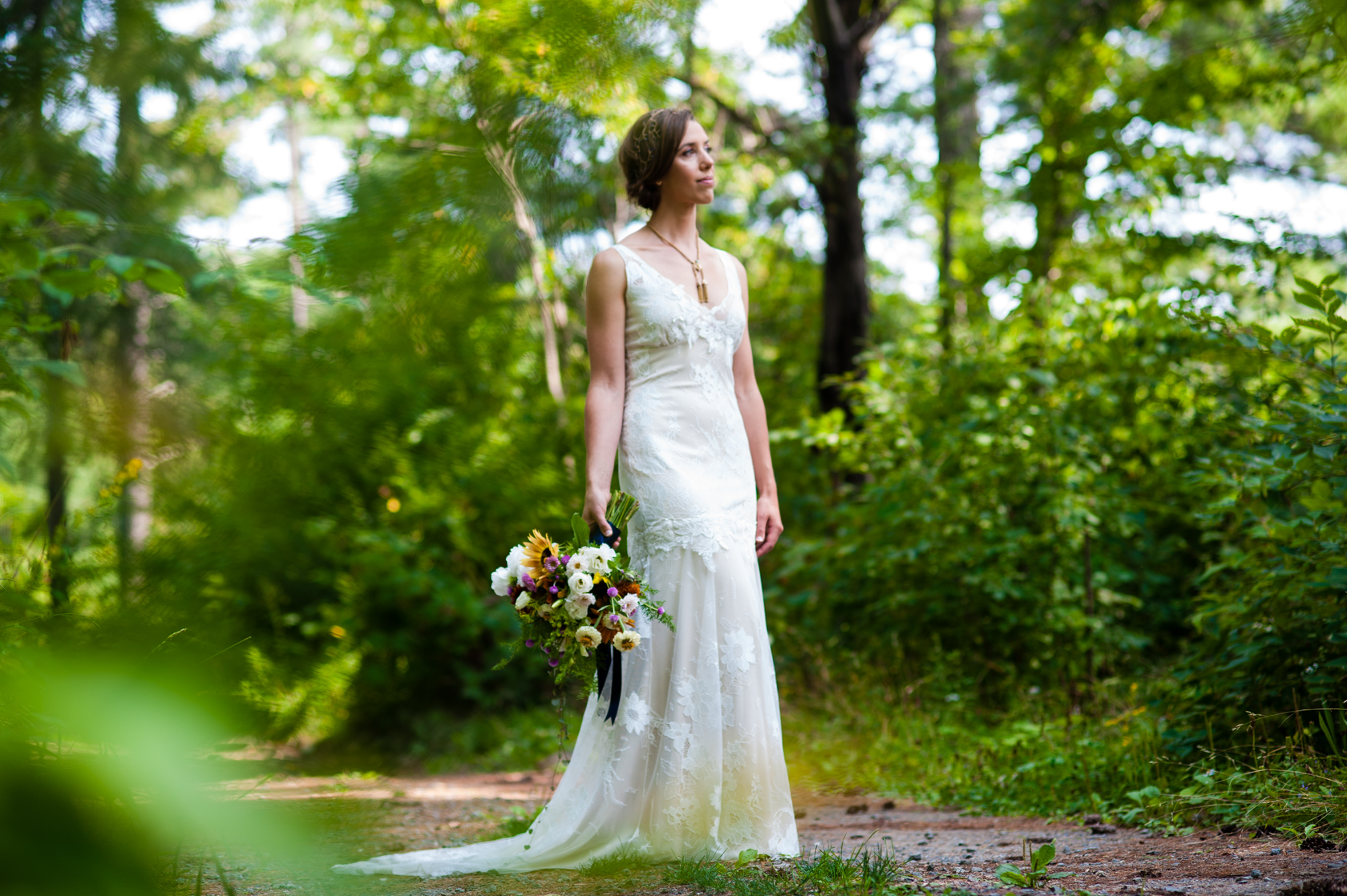 gorgeous bride in lace gown holding a wildflower bouquet in the woods