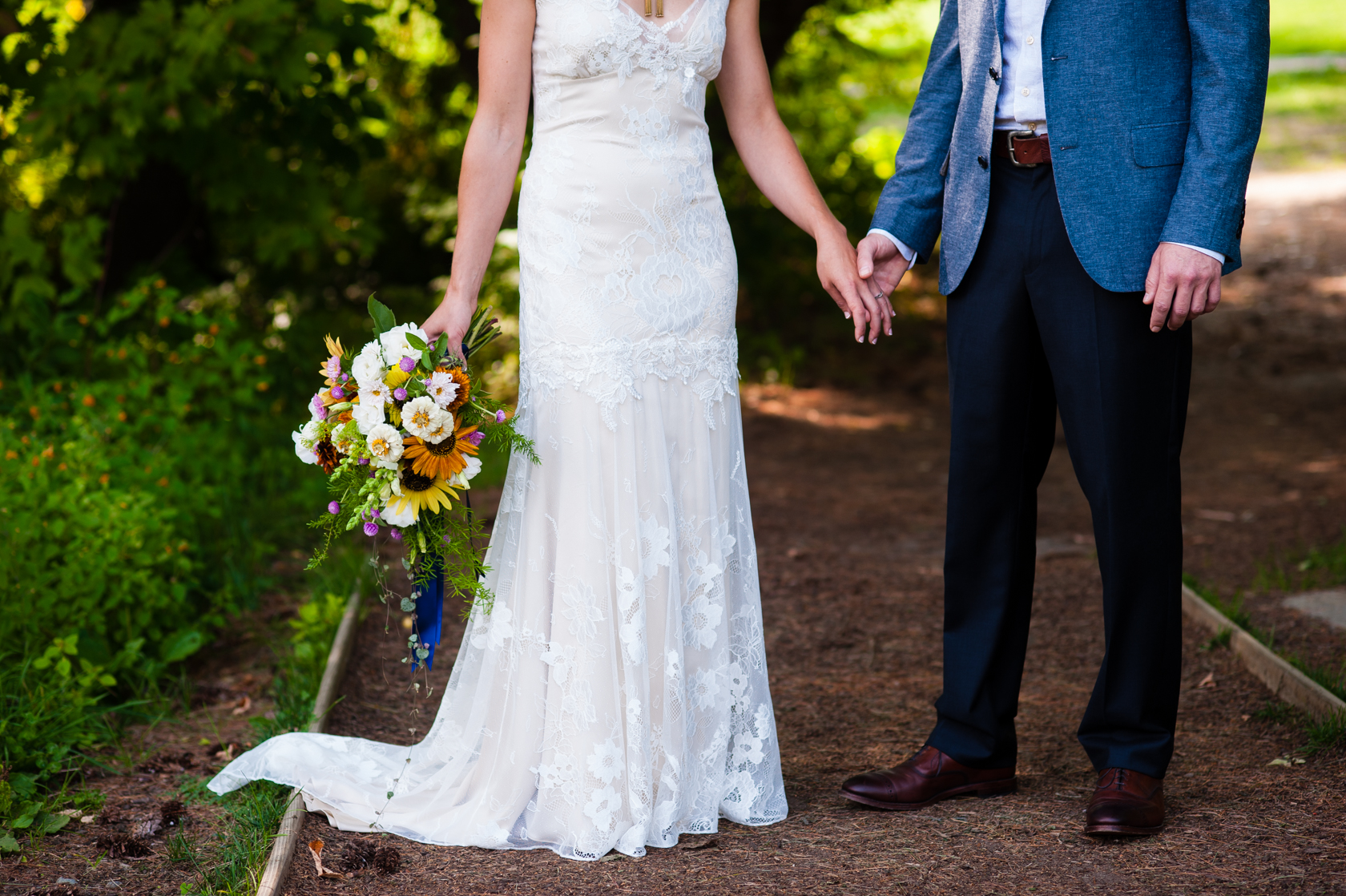 bride in gorgeous lace dress and groom in grey suit hold hands