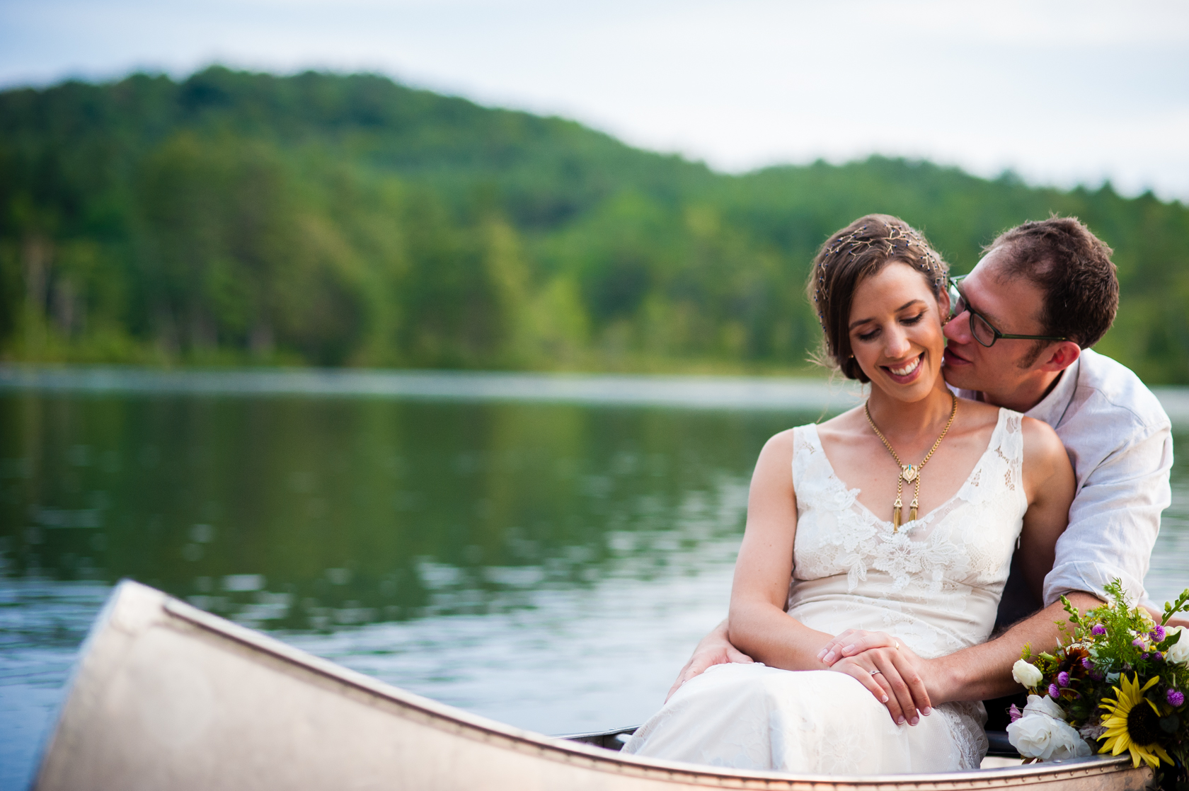 groom gives his bride a kiss on the cheek during their post wedding canoe paddle on the lake 