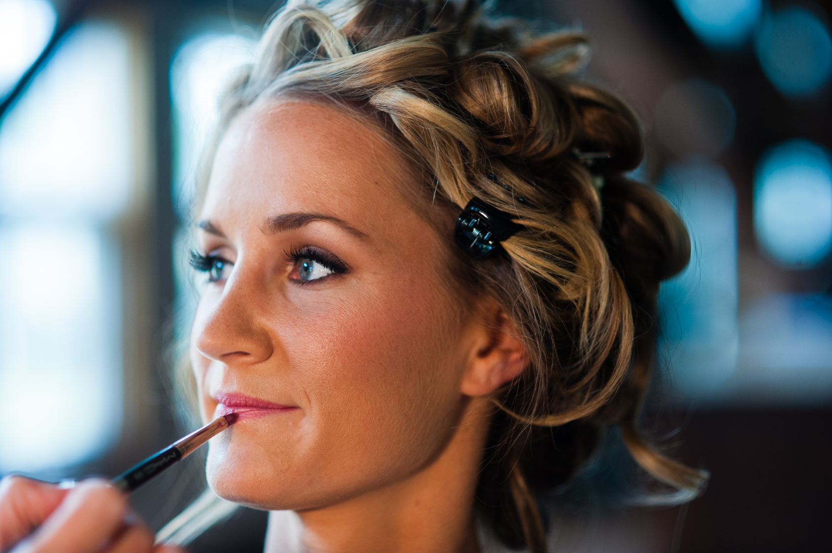 beautiful blonde bride getting her makeup done before her rustic farm wedding 