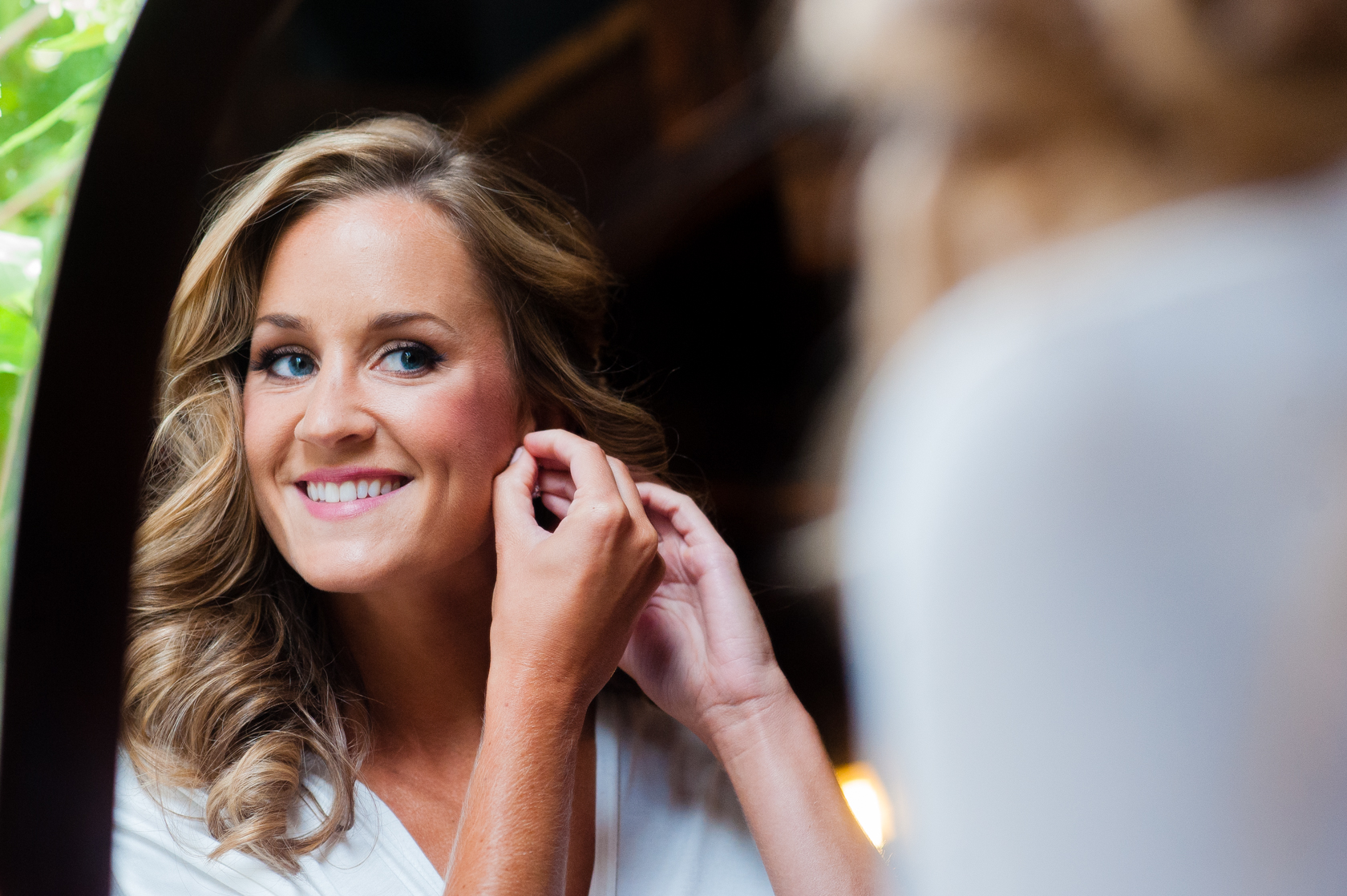 beautiful bride puts her earrings on in the mirror 