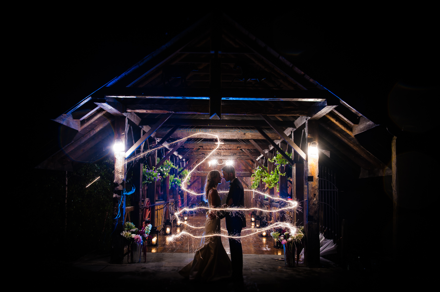 bride and groom stand in the center of a ring of sparklers in front of their gorgeous barn wedding venue 