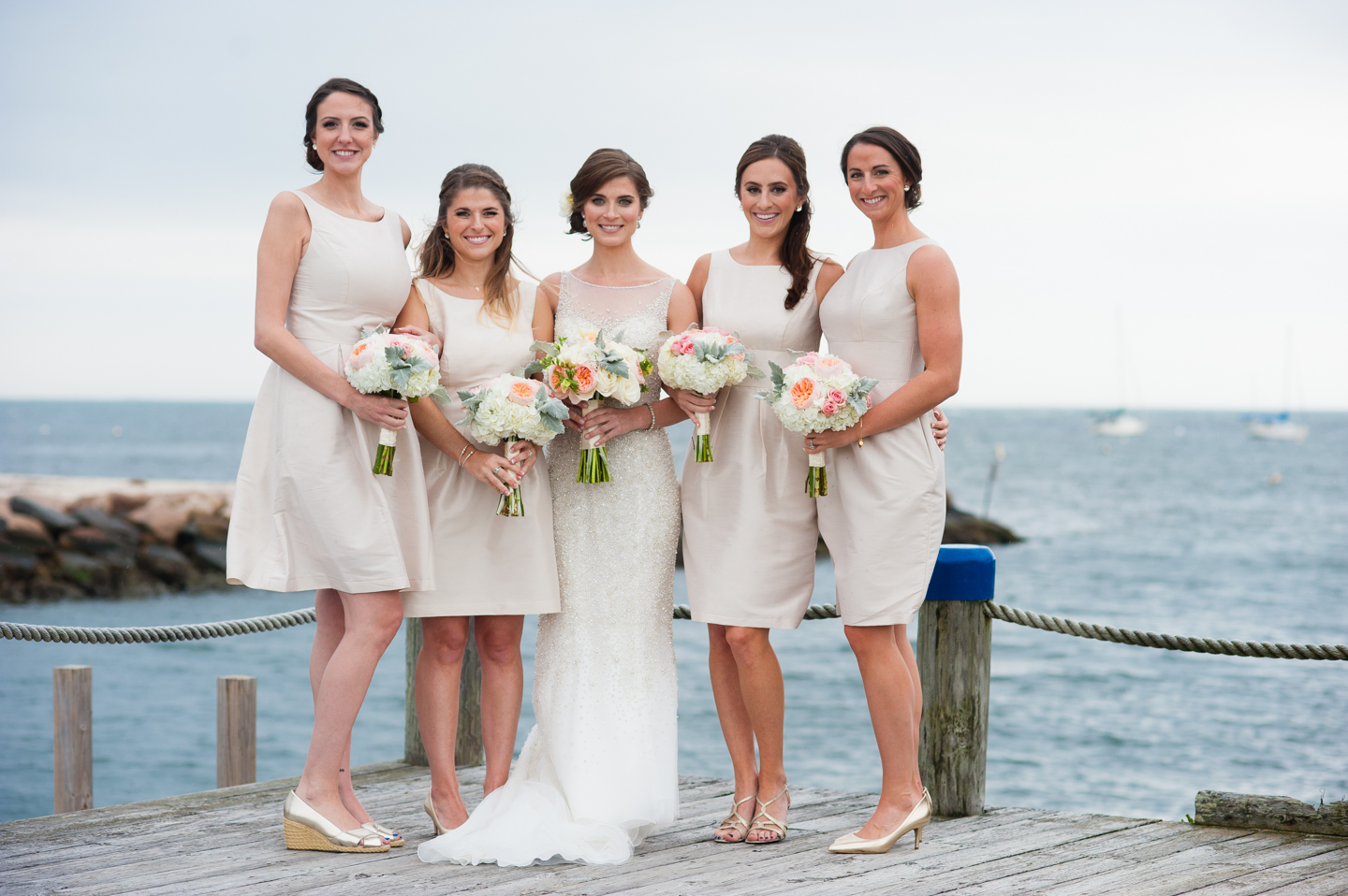 beautiful bridesmaids in classic cream dresses stand by the ocean 