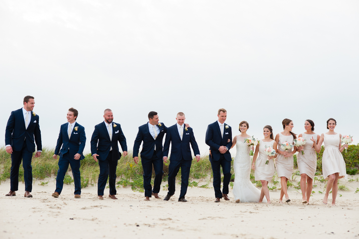 fun wedding party walks through the sand on the beach laughing 