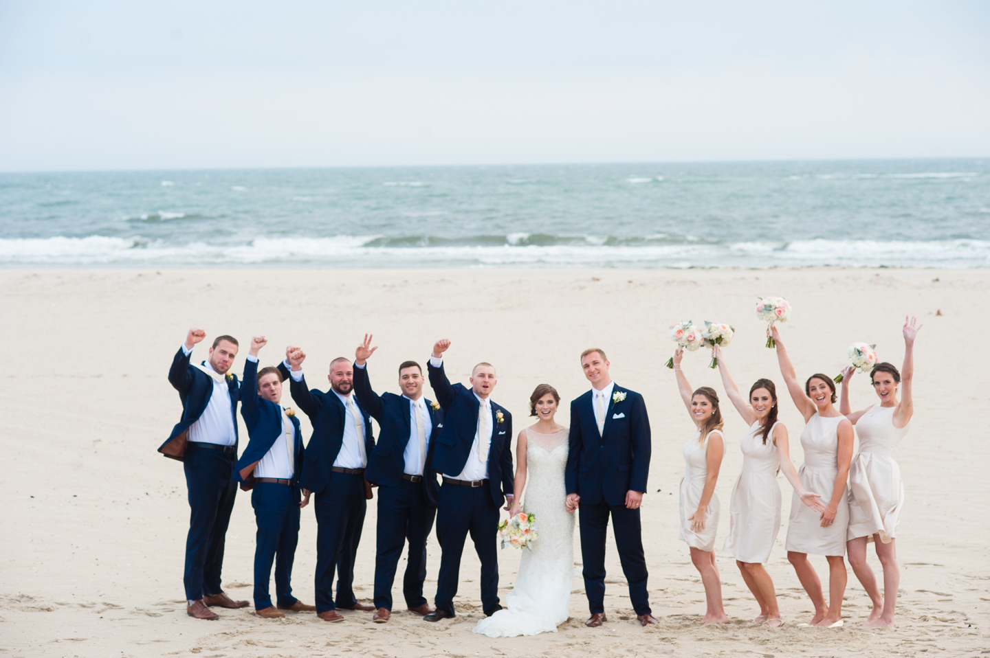 bride and groom cheer with their wedding party with the ocean behind 