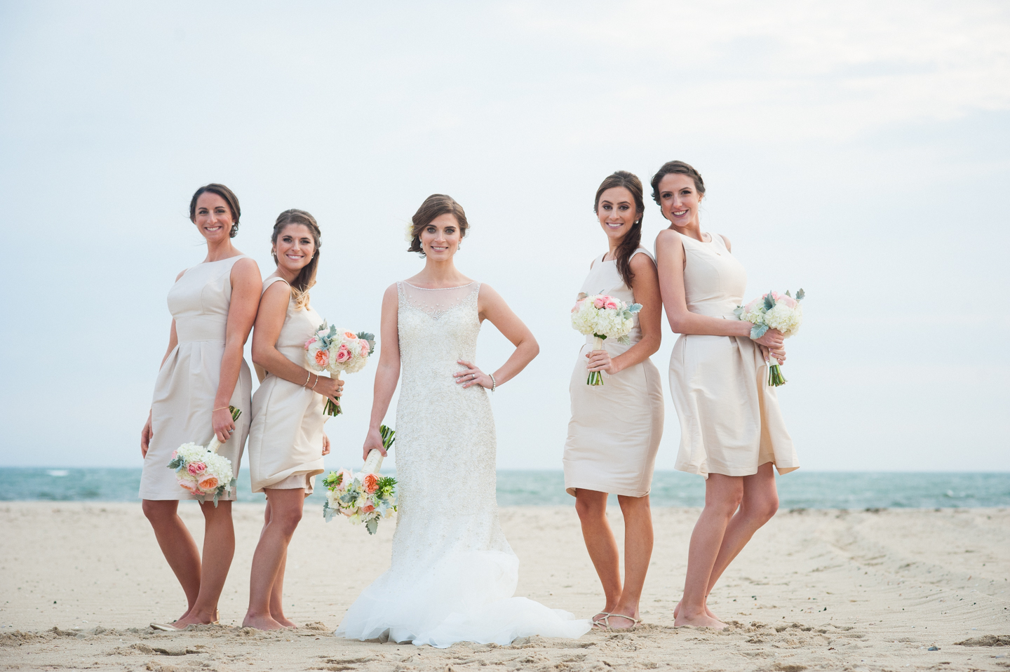 bride and her bridesmaids stand by the ocean in gorgeous white and cream dresses