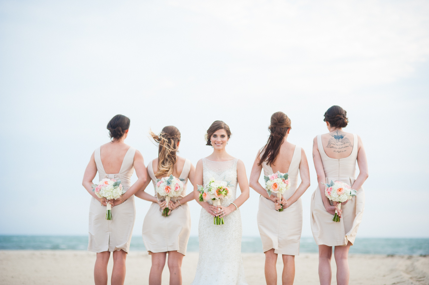 beautiful bride faces camera while her bridesmaids show off their flowers and the backs of their dresses