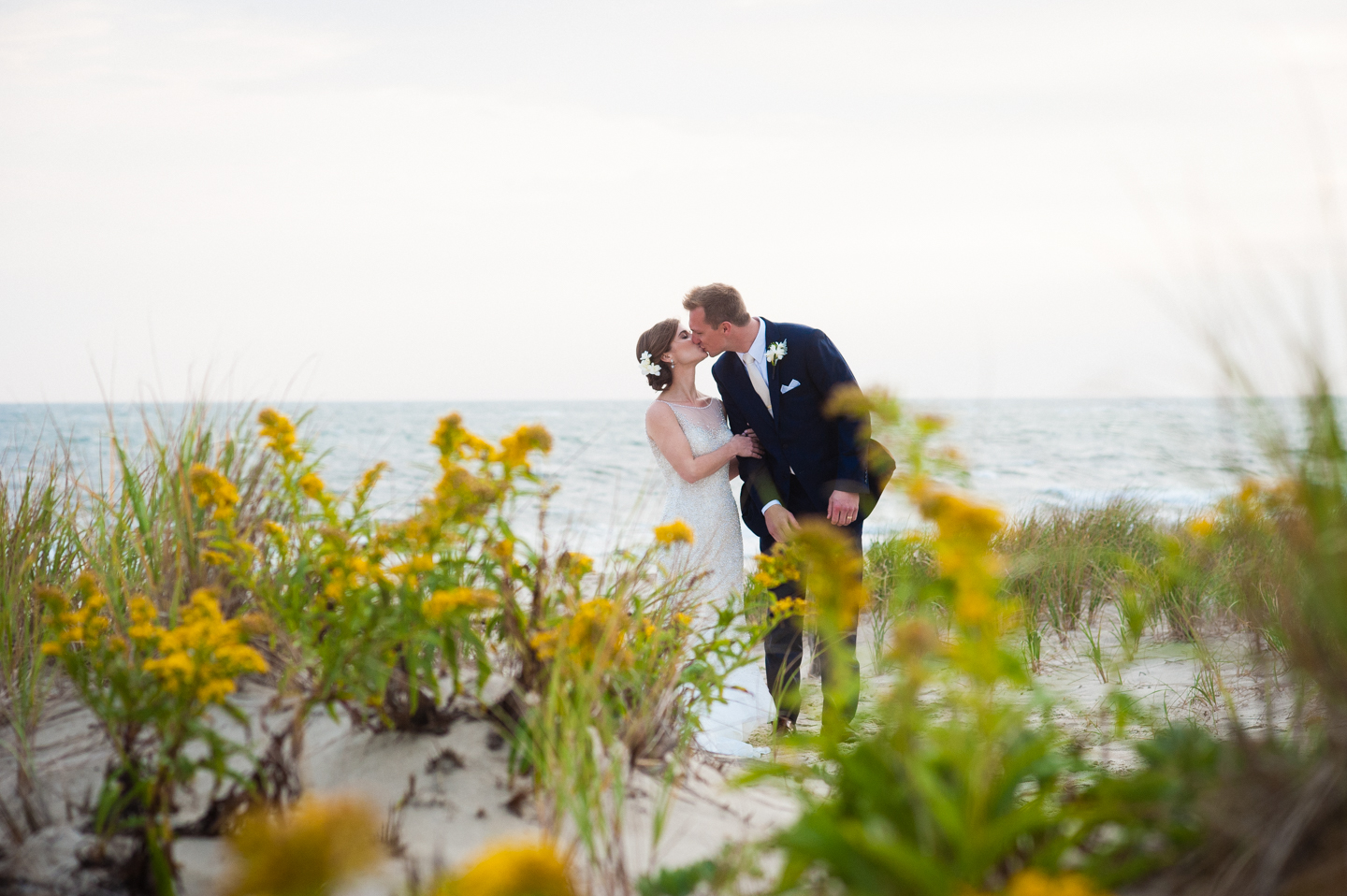 newly married couple kisses by the ocean with yellow flowers all around 