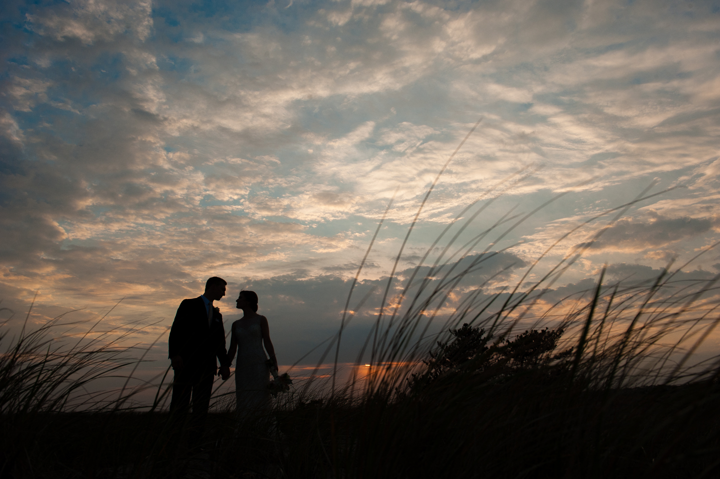bride and groom lean in for a kiss with dark sunset sky behind 