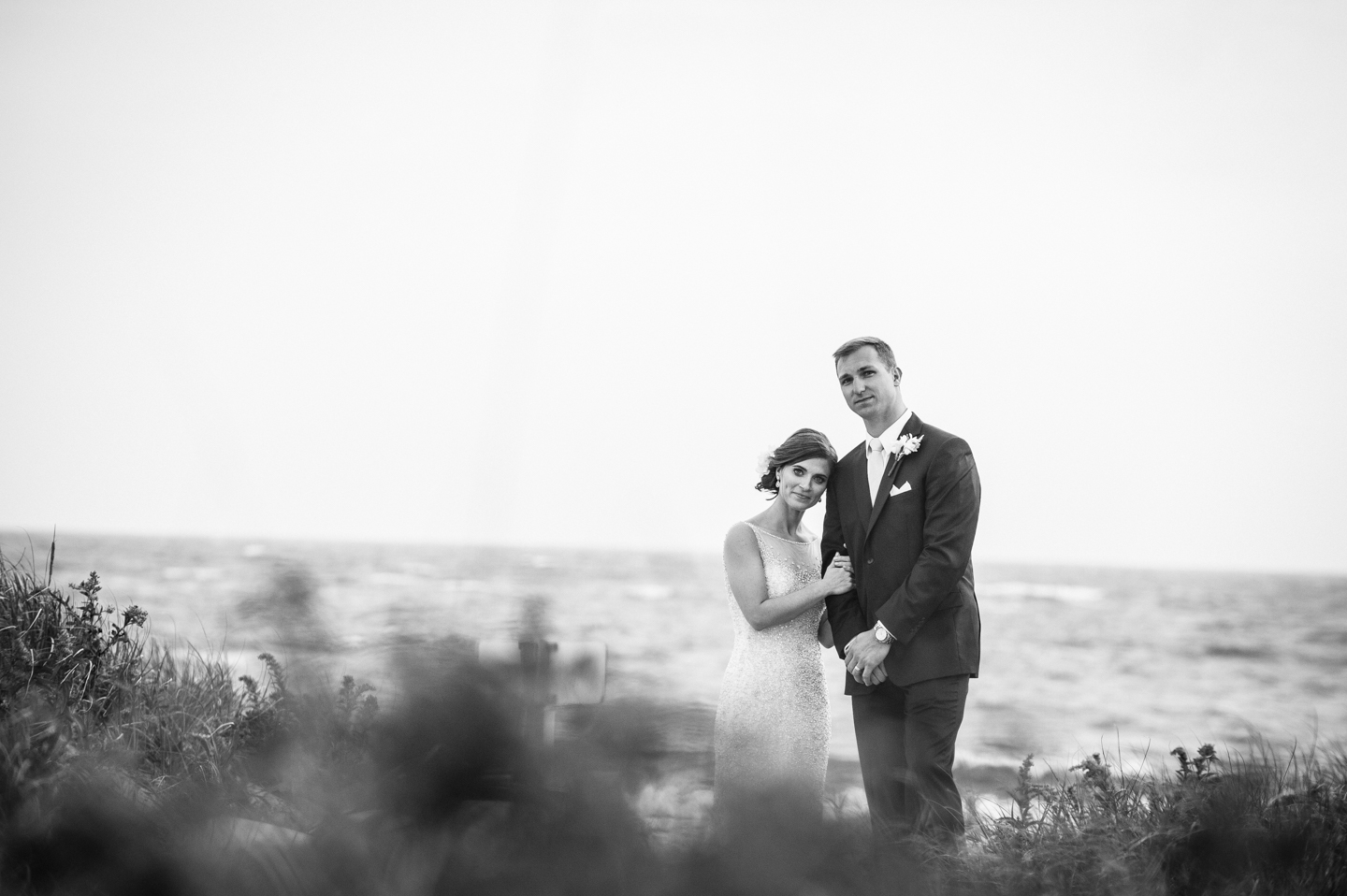 bride rests her head on her husbands shoulder with stormy sea behind them