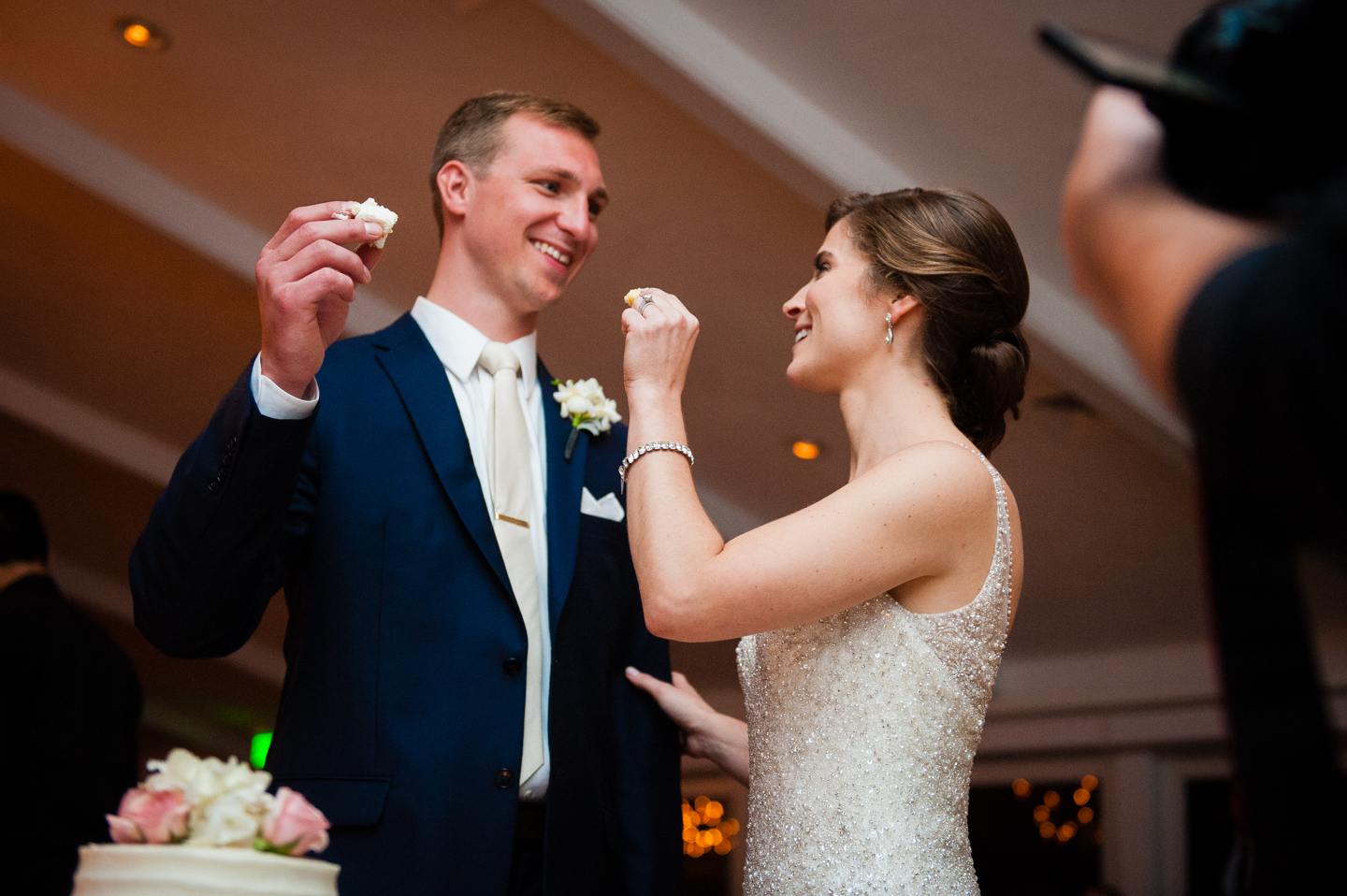 bride and groom laughing as they feed each other wedding cake