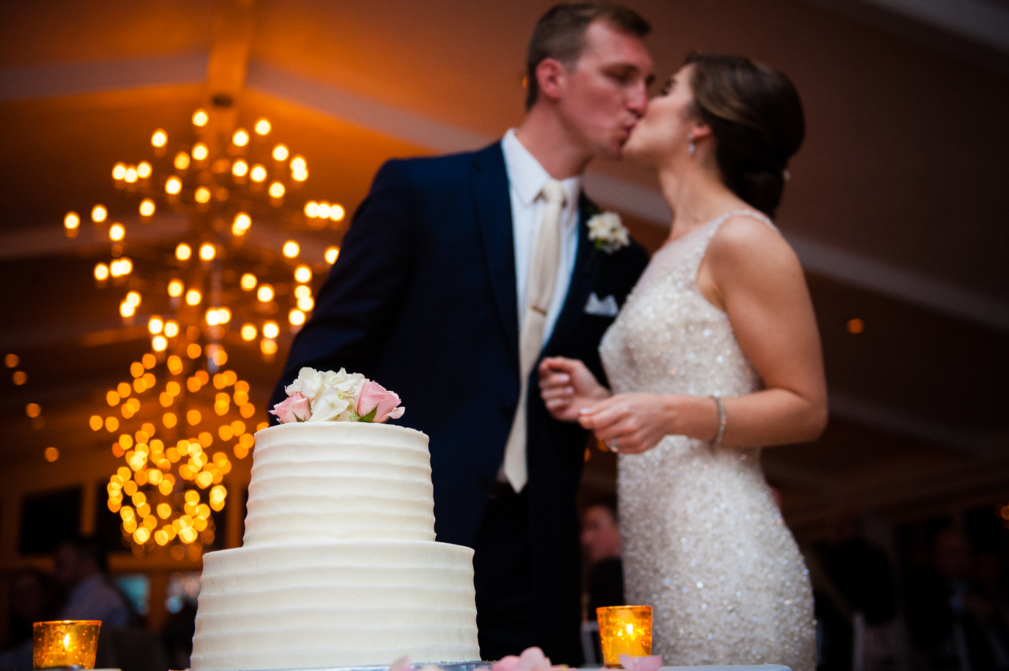 newly married couple kisses behind their classic white wedding cake 