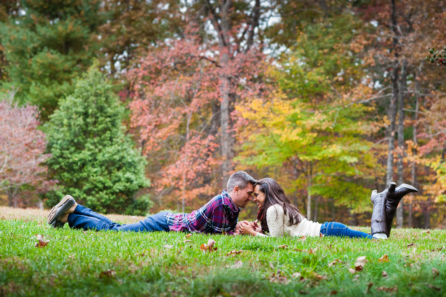 young couple arm wrestles during fall engagement at nc arboretum 