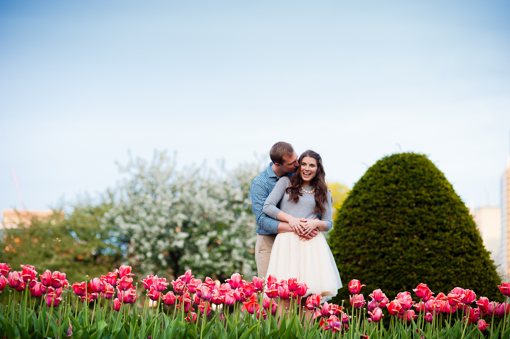 adorable couple poses in red tulips during their spring engagement session