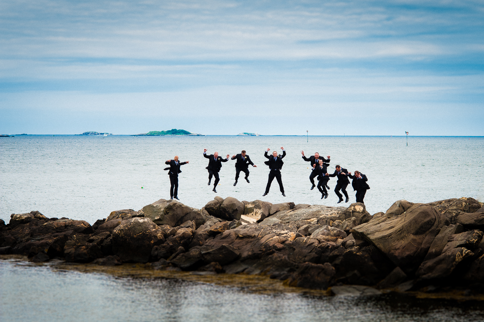 adventurous groomsmen jump on rocks in ocean
