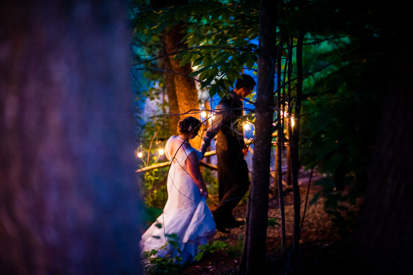 bride and groom walk hand in hand down dimly lit wooded path 